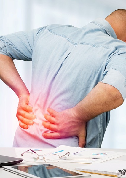 Man with back pain standing near his desk